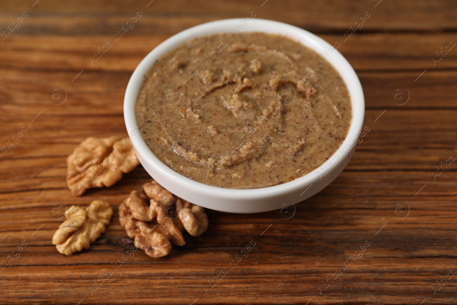 Photo of Delicious nut butter in bowl and walnuts on wooden table, closeup