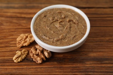 Delicious nut butter in bowl and walnuts on wooden table, closeup