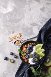 Photo of Tasty granola with yogurt, blueberries and kiwi in bowl on gray textured table, flat lay. Space for text