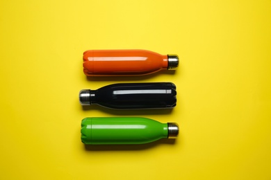 Photo of Modern thermo bottles on yellow background, flat lay