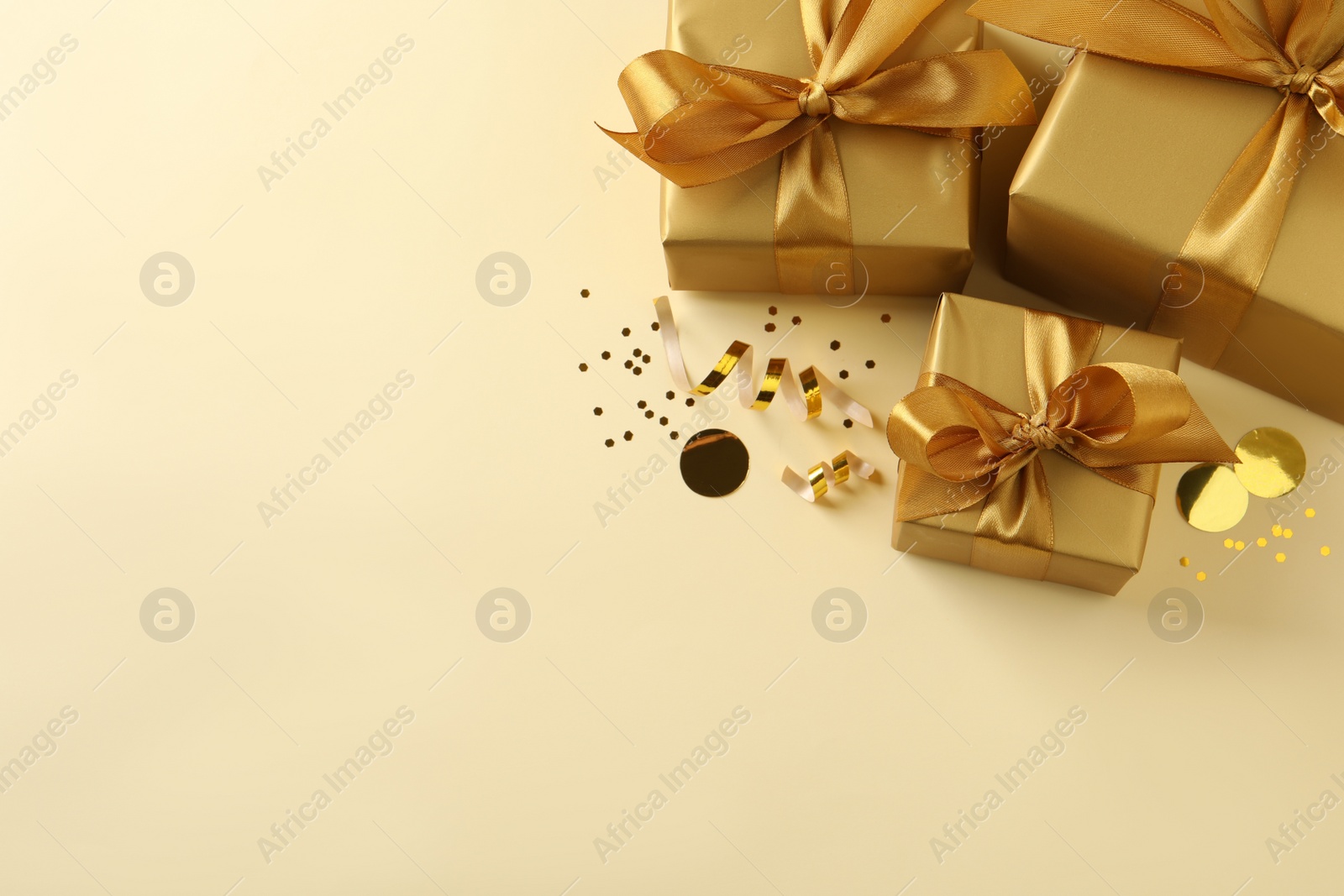 Photo of Beautifully wrapped gift boxes and confetti on beige background, flat lay. Space for text