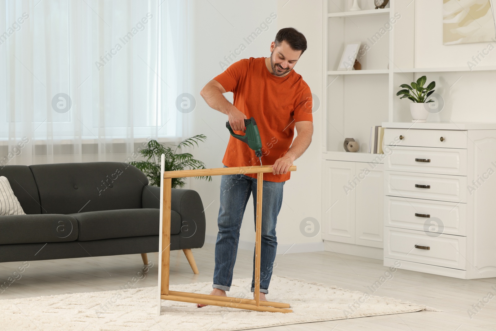 Photo of Man with electric screwdriver assembling shoe storage bench at home