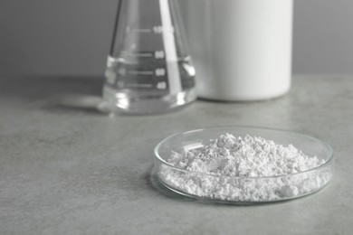Photo of Petri dish with calcium carbonate powder on light grey table. Space for text
