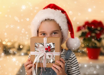 Cute little girl in Santa hat with gift from Christmas advent calendar at home. Bokeh effect