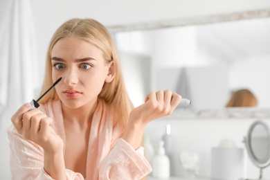 Photo of Emotional woman holding mascara brush with fallen eyelashes indoors