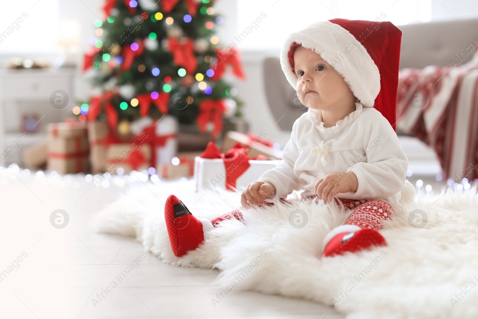 Photo of Cute baby in Santa hat on floor at home. Christmas celebration