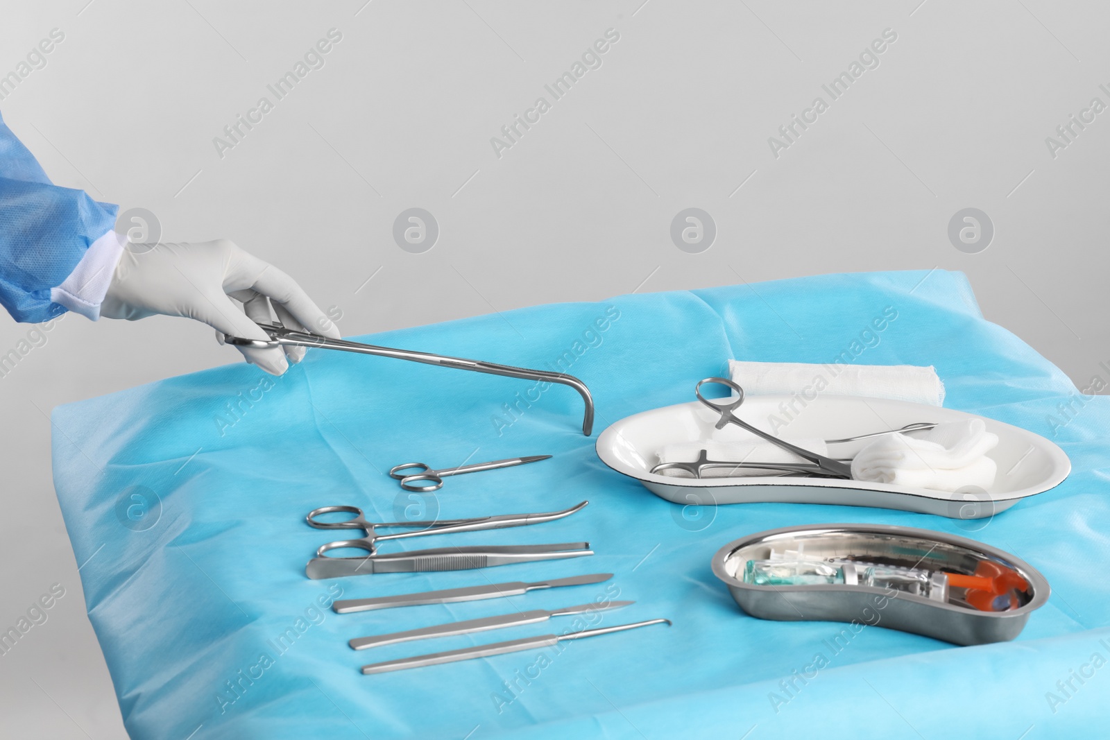 Photo of Doctor holding forceps over table with surgical instruments against light background, closeup