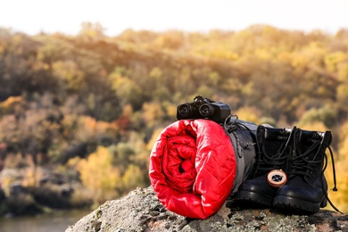 Photo of Set of camping equipment with sleeping bag on rock outdoors. Space for text