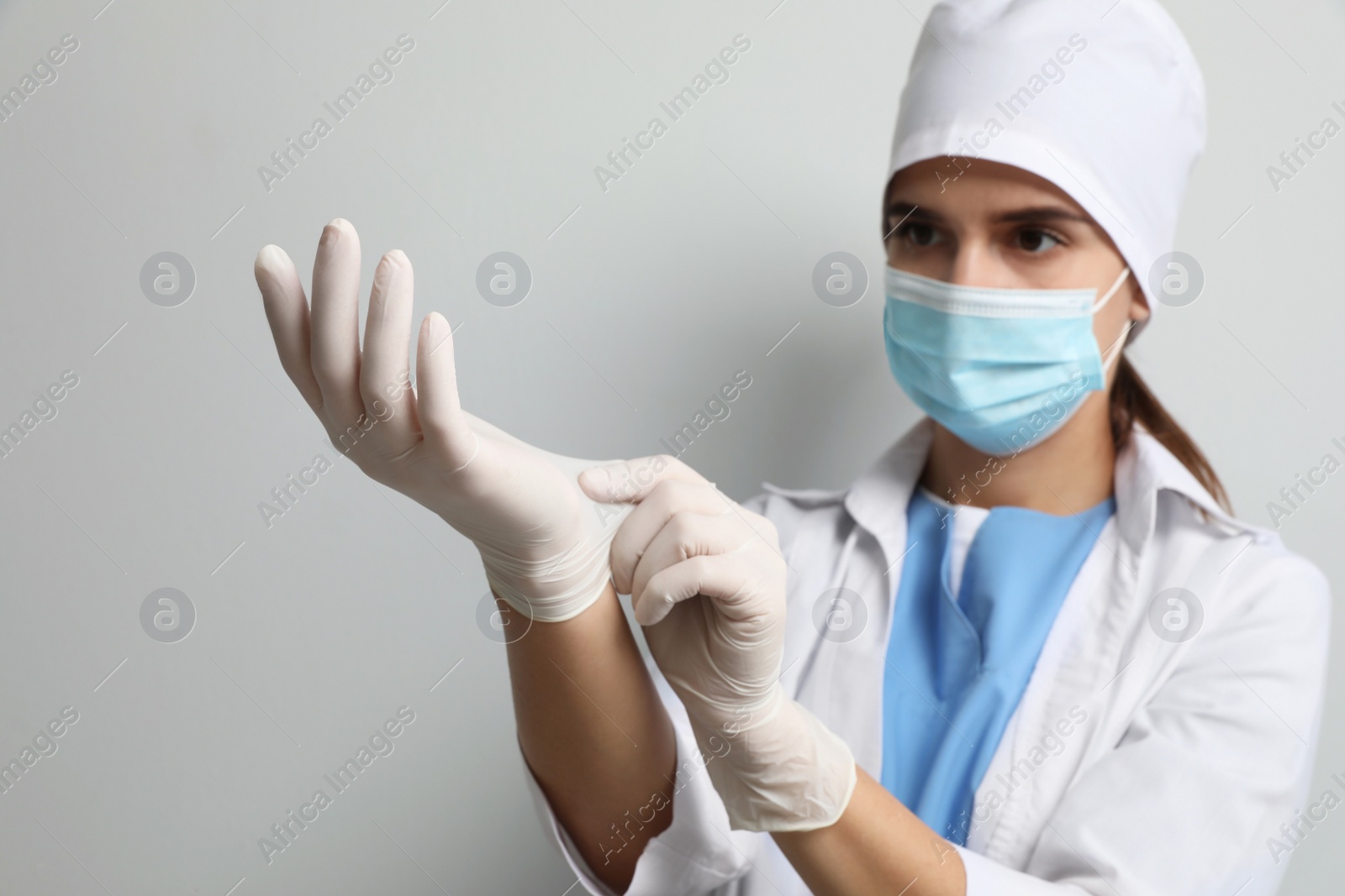 Photo of Doctor in protective mask putting on medical gloves against light grey background