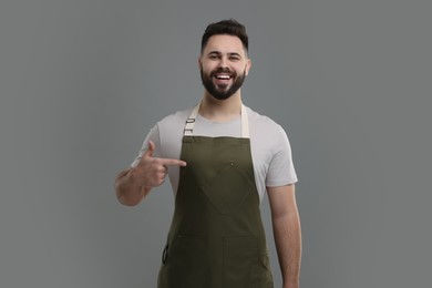 Photo of Smiling man pointing at kitchen apron on grey background. Mockup for design