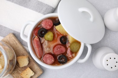 Photo of Meat solyanka soup with thin dry smoked sausages in pot on light table, flat lay