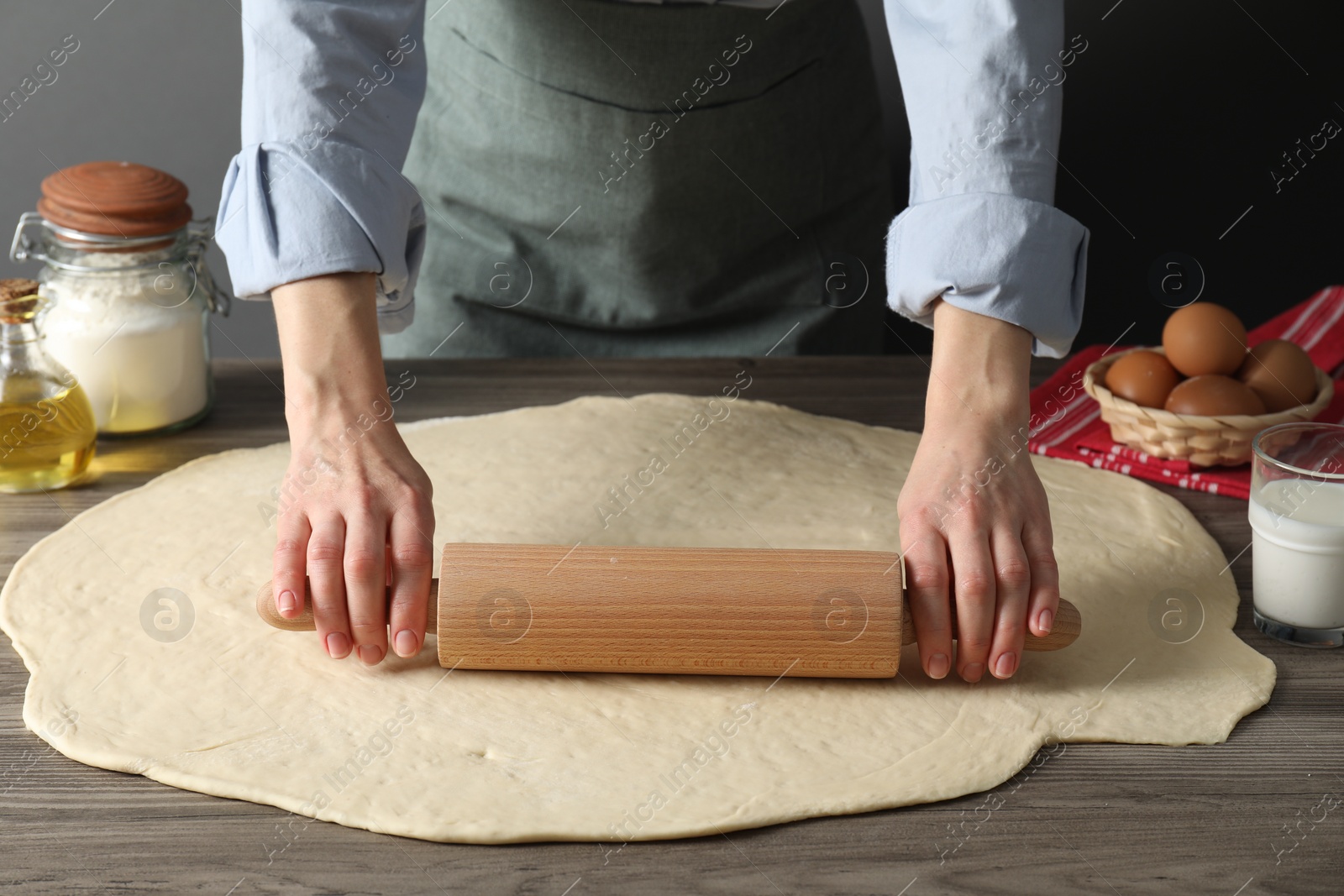 Photo of Woman rolling raw dough at wooden table, closeup