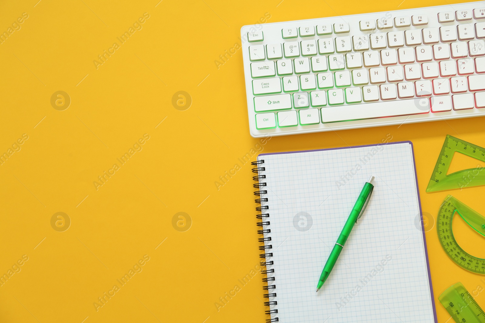 Photo of Modern keyboard with RGB lighting and stationery on yellow background, flat lay. Space for text