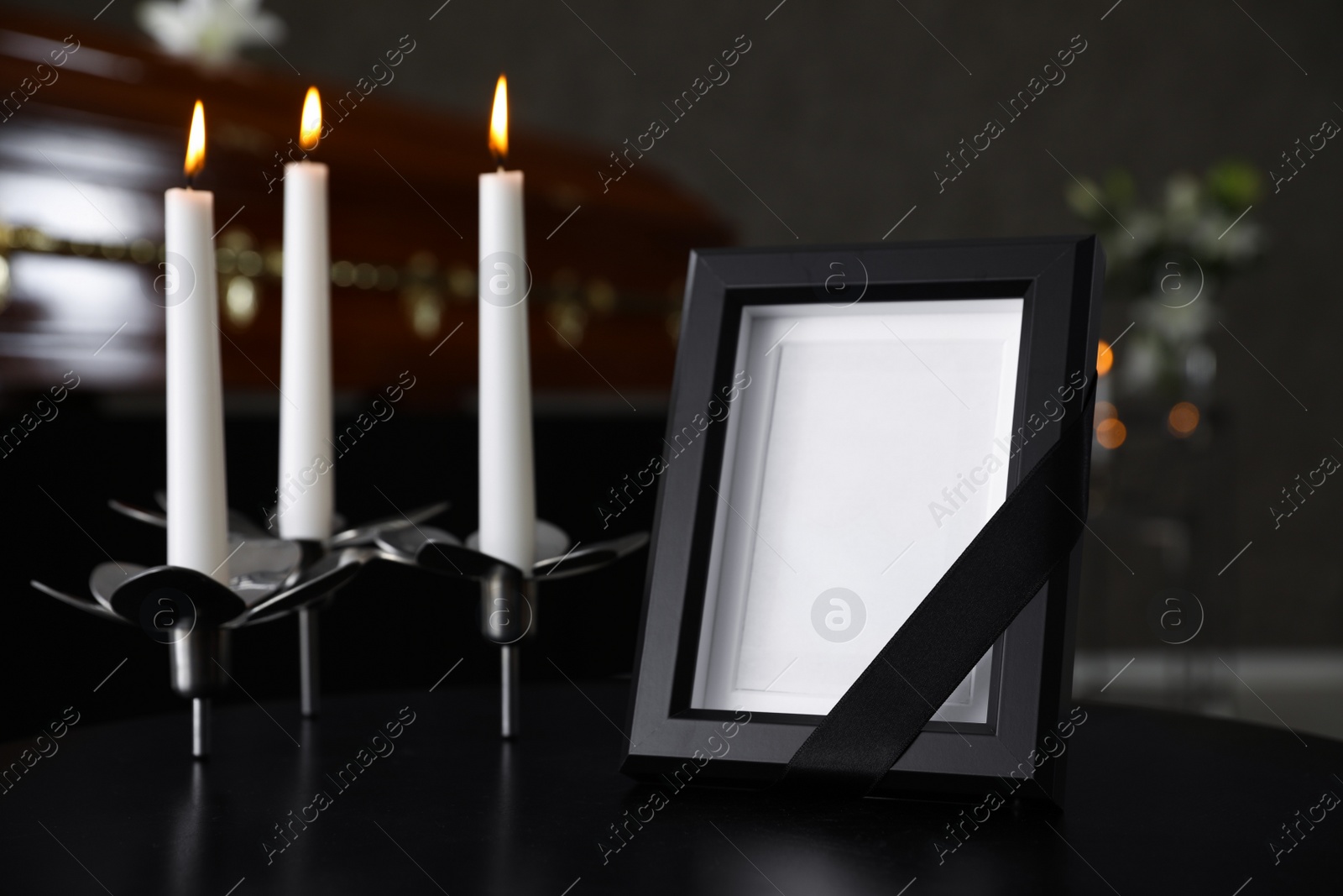 Photo of Black photo frame with burning candles on table in funeral home