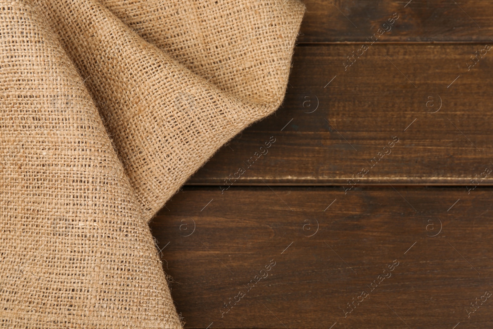 Photo of Brown burlap fabric on wooden table, top view. Space for text