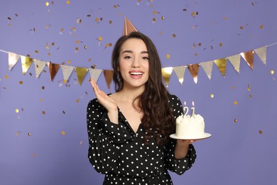 Coming of age party - 21st birthday. Smiling woman holding delicious cake with number shaped candles on violet background