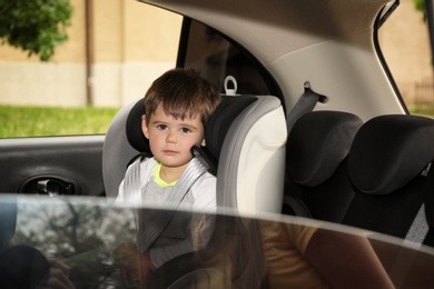 Photo of Sad little boy sitting in safety seat alone  inside car. Child in danger