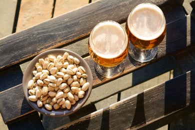 Photo of Glasses of cold beer and pistachios on wooden bench, flat lay