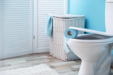 Toilet bowl with paper roll in bathroom. Space for text