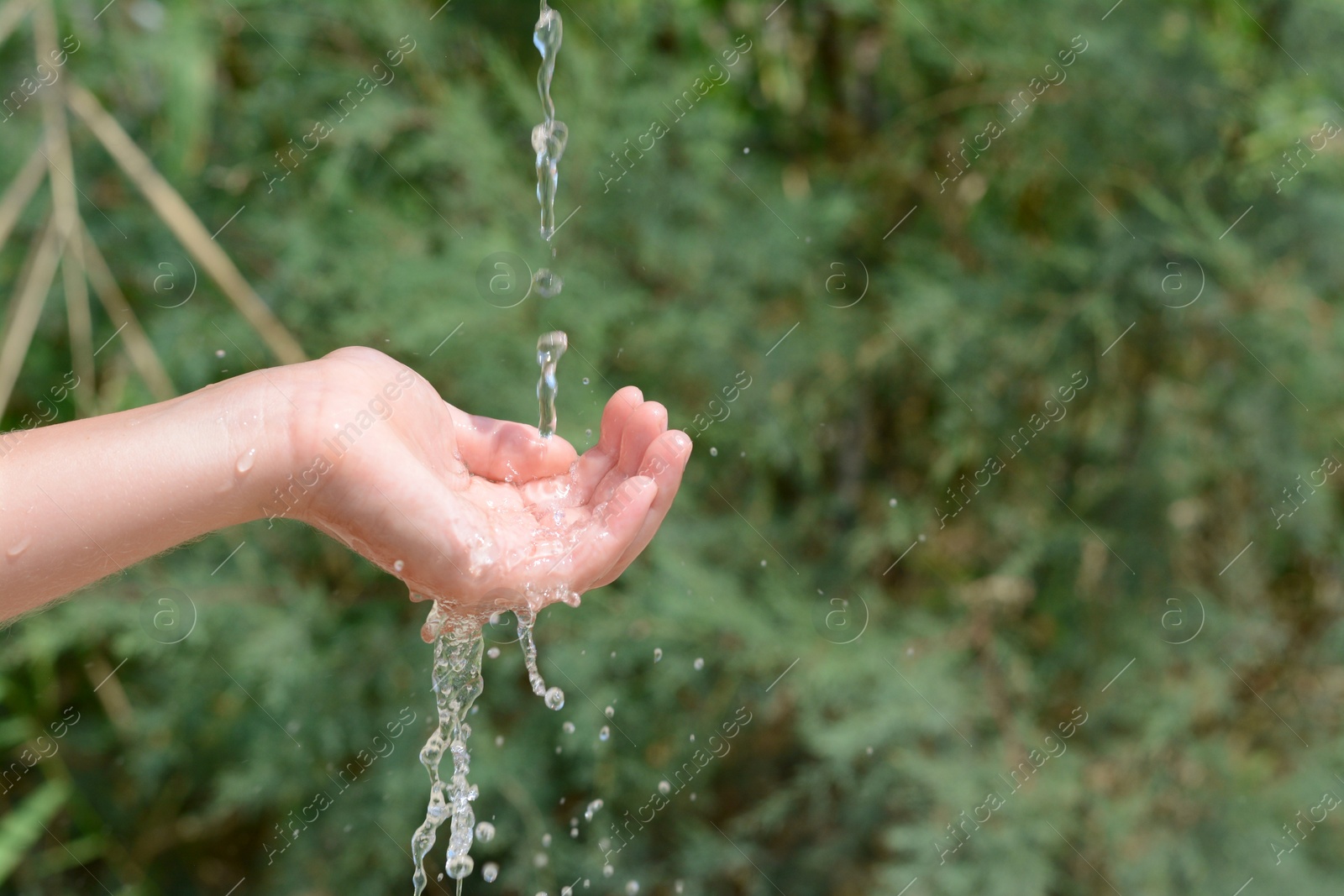 Photo of Pouring water into kid`s hand outdoors, closeup. Space for text