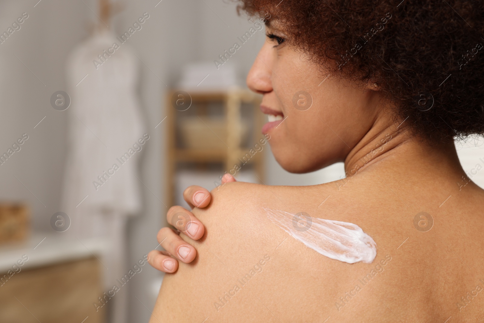 Photo of Beautiful young woman applying body cream onto back in bathroom, closeup. Space for text