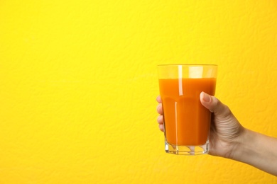 Photo of Woman holding glass of carrot juice on color background, closeup with space for text