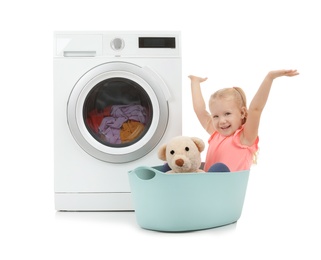 Photo of Cute little girl with teddy bear sitting in laundry basket near washing machine