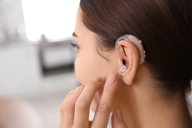 Young woman adjusting hearing aid indoors, closeup