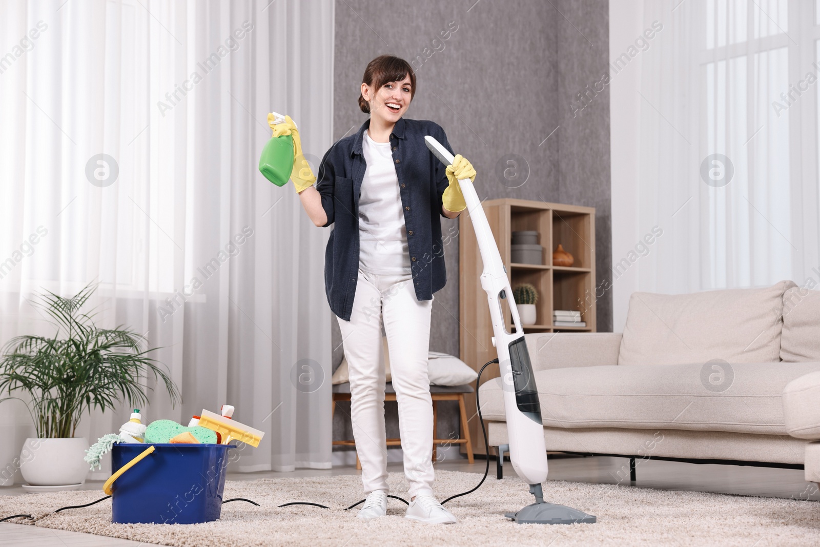 Photo of Happy young housewife with spray bottle having fun while cleaning carpet at home