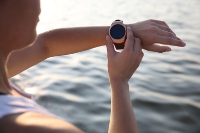 Photo of Woman checking fitness tracker after training near river, closeup