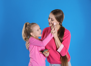 Photo of Happy daughter applying powder onto mother's face on blue background