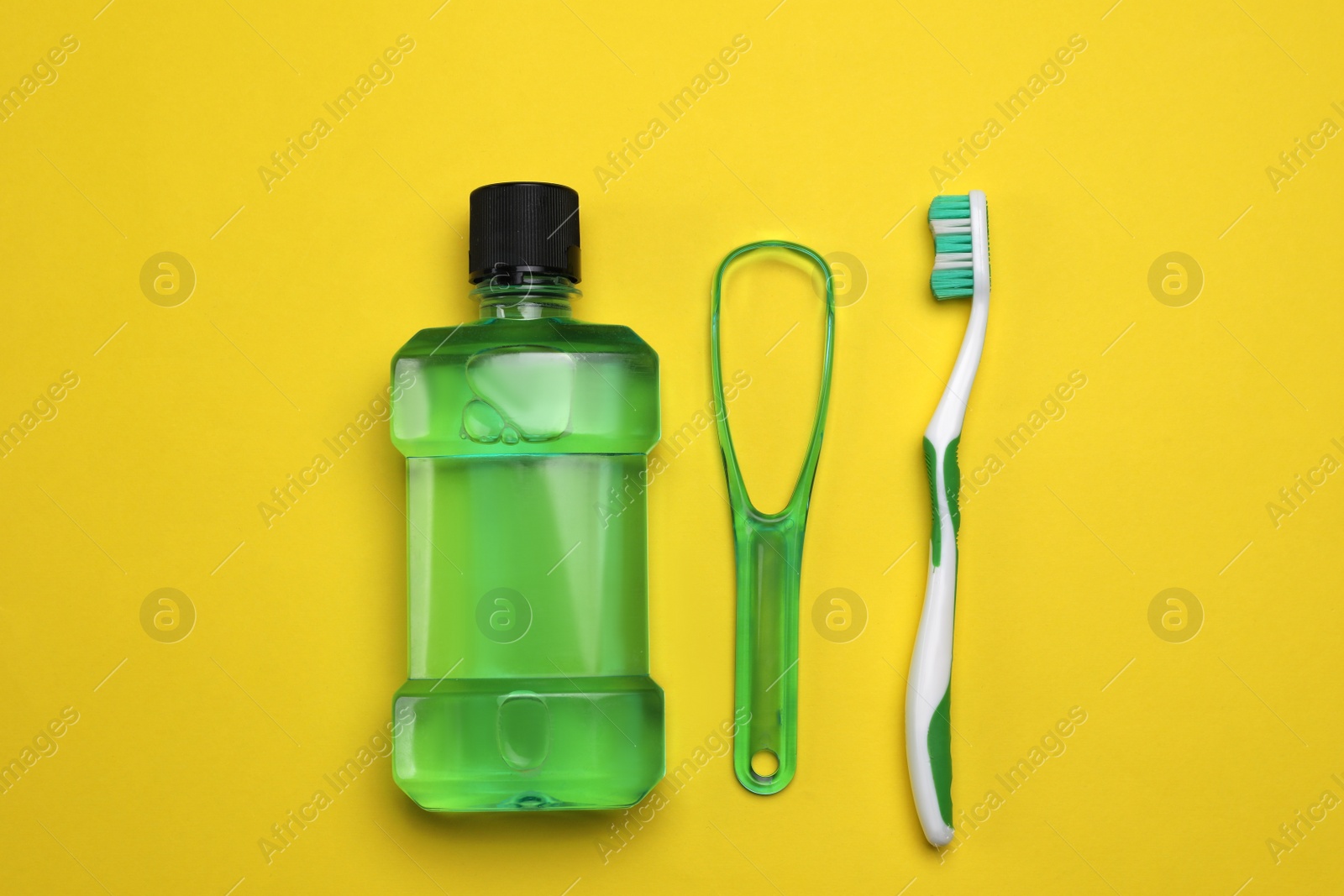 Photo of Tongue cleaner, mouthwash and toothbrush on yellow background, flat lay