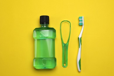 Photo of Tongue cleaner, mouthwash and toothbrush on yellow background, flat lay