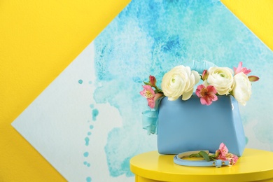 Photo of Elegant handbag with flowers and belt on table against color background, space for text