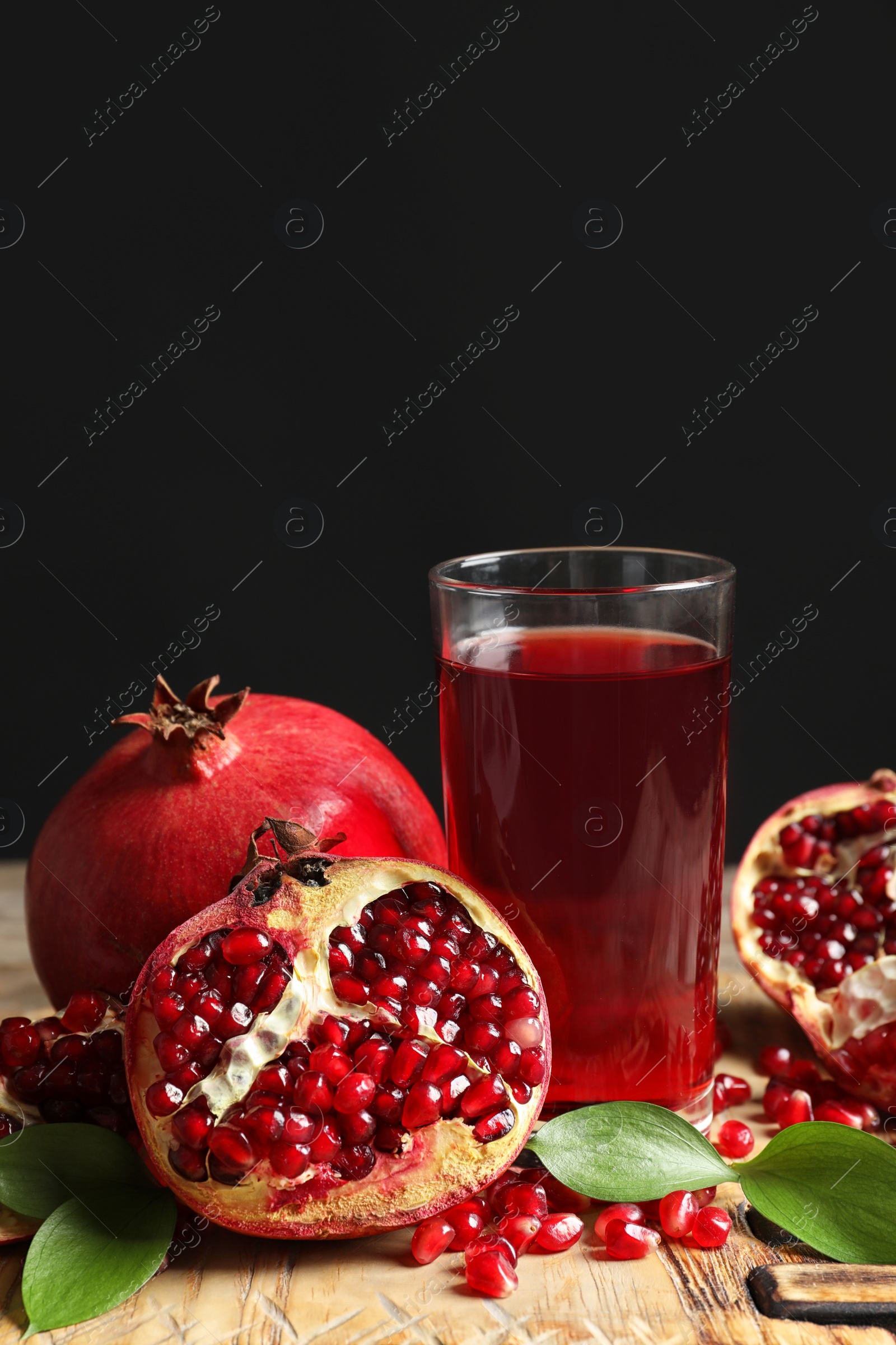 Photo of Glass of pomegranate juice and fresh fruits on wooden board against black background