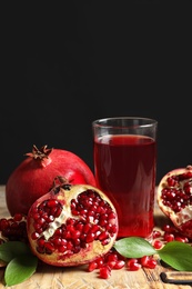 Glass of pomegranate juice and fresh fruits on wooden board against black background