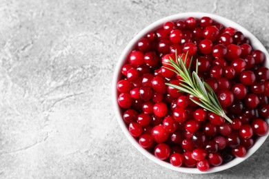 Photo of Fresh ripe cranberries and rosemary in bowl on grey table, top view. Space for text
