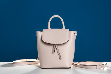 Photo of Stylish woman's bag on white table against blue background