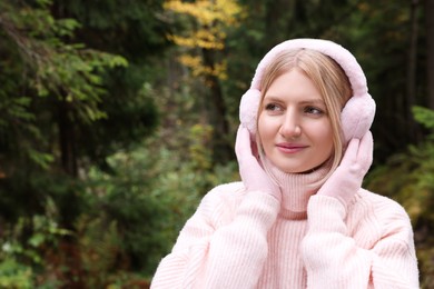 Young beautiful woman wearing warm earmuffs in forest