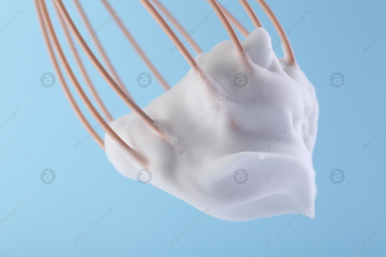 Photo of Whisk with whipped cream on light blue background, closeup