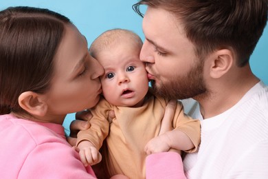 Photo of Happy family. Parents kissing their cute baby on light blue background