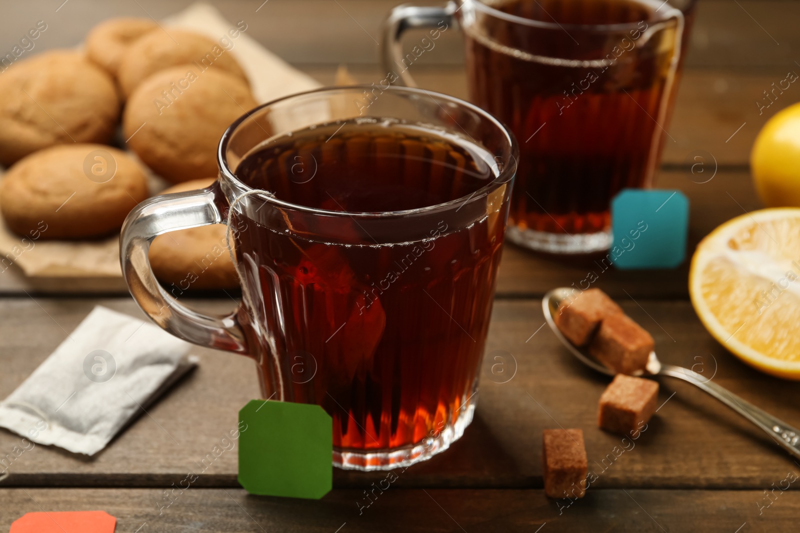 Photo of Tea bags in glass cups of hot water and sugar cubes 
on wooden table