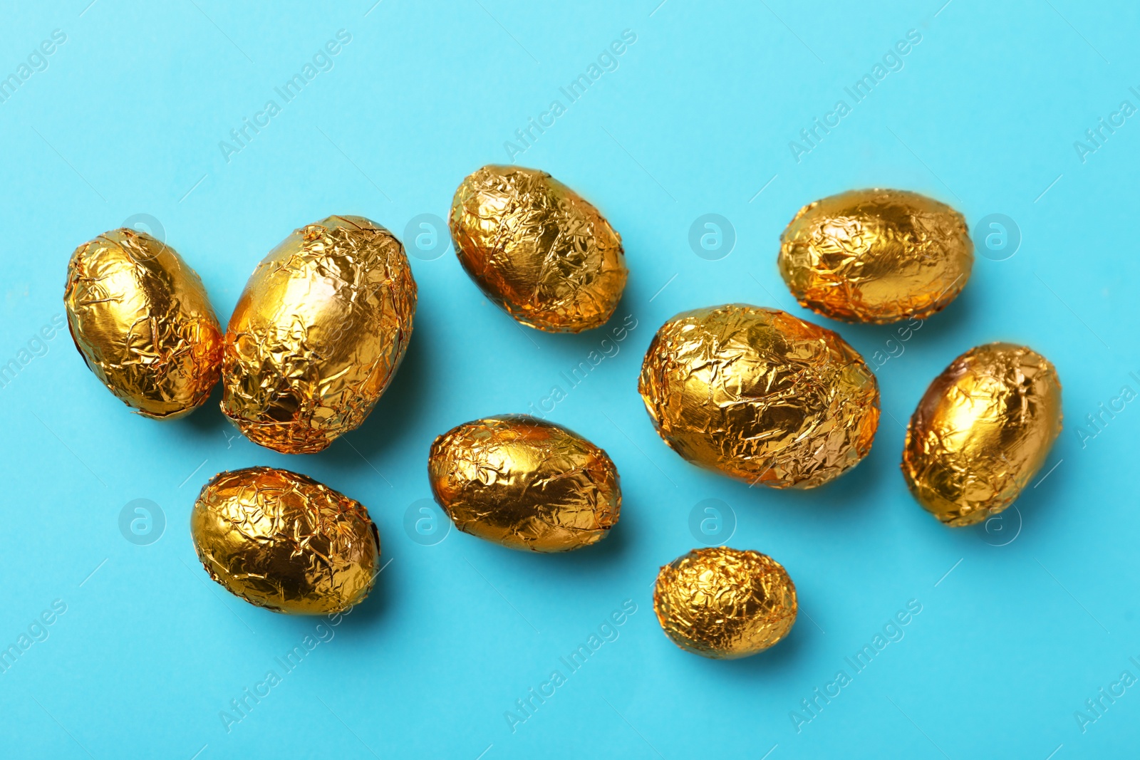 Photo of Chocolate eggs wrapped in golden foil on light blue background, flat lay