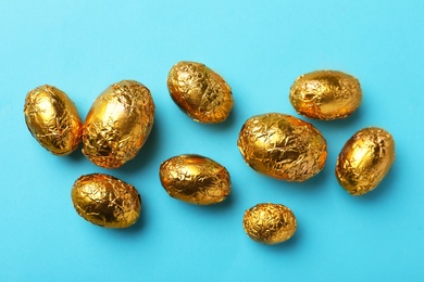 Chocolate eggs wrapped in golden foil on light blue background, flat lay