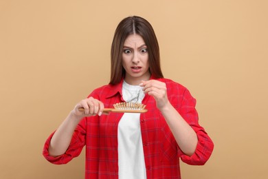 Photo of Emotional woman untangling her lost hair from brush on beige background. Alopecia problem