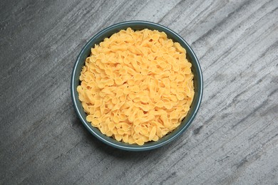 Raw farfalline pasta in bowl on grey table, top view