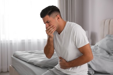 Photo of Man suffering from nausea on bed at home. Food poisoning