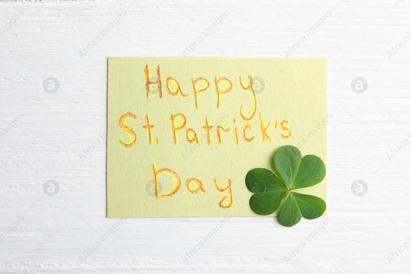 Photo of Clover leaf and note with text HAPPY ST. PATRICK'S DAY on white wooden table, flat lay