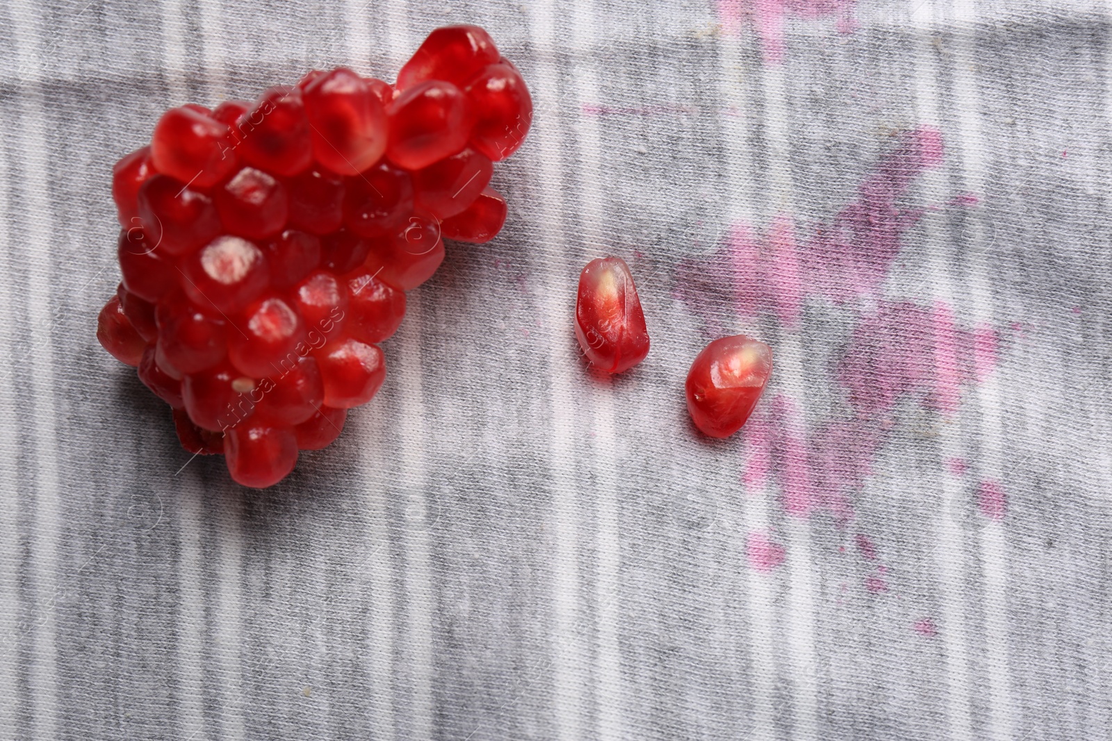 Photo of Shirt with fruit juicy stains and pomegranate seeds as background, top view