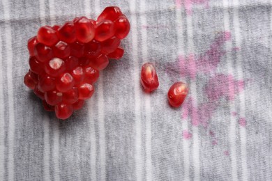 Shirt with fruit juicy stains and pomegranate seeds as background, top view